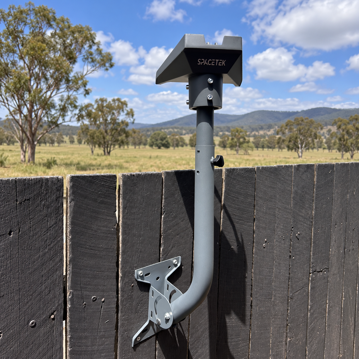 Grey Spacetek adjustable Starlink wall mount attached to a timber fence, with rural paddocks and eucalyptus trees in the background.