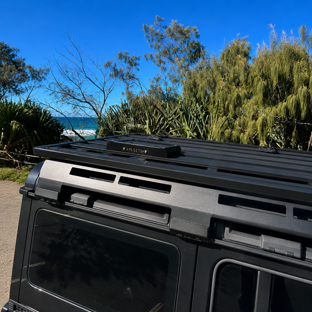 Spacetek Stealth Mount for Starlink Mini installed on a Rhino-Rack platform roof rack, showcasing a low-profile black aluminium design mounted on a touring vehicle with an ocean backdrop.
